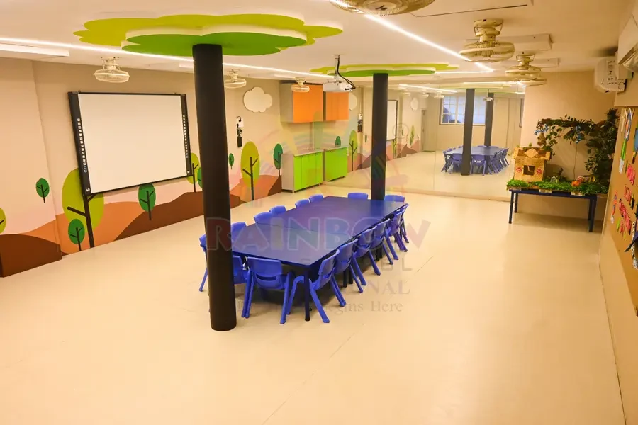 Blue child-sized tables and a tree-themed mural in a Rainbow Preschool activity room