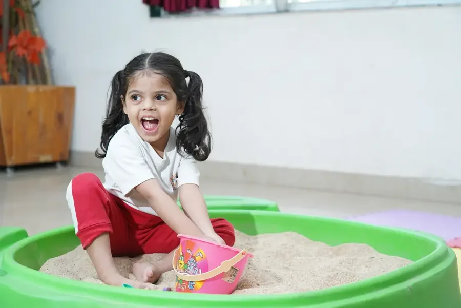Child playing with a pink bucket in a green sensory sand tray