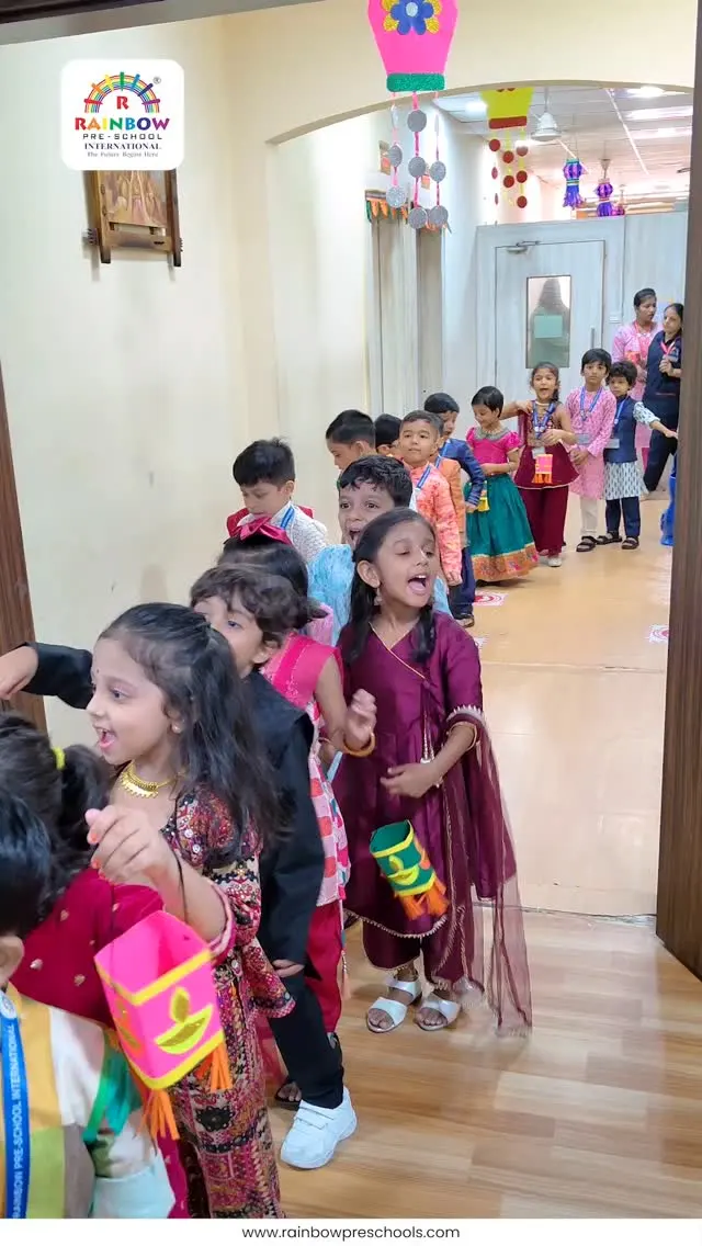 Children in festive clothing carry paper lanterns through a decorated school hallway